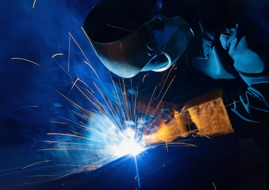 Close-up of a welder repairing a machinery component, sparks lighting the workshop
